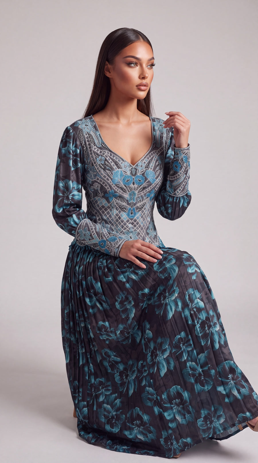 Sadil floral print maxi dress with V-neck, long sleeves, and pleated skirt in charcoal and teal on a seated model.